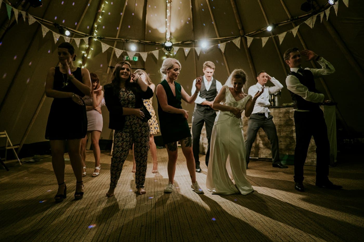 Wedding guests dancing in a tent strung with lights